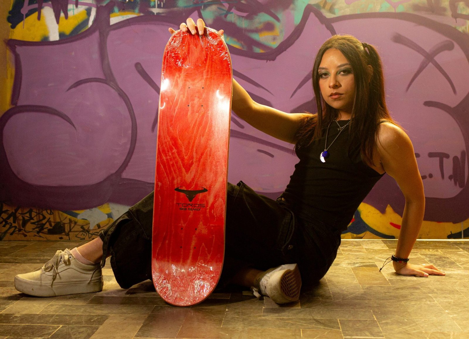 A skater girl poses with her skateboard against a colorful graffiti wall in Toluca de Lerdo, Mexico.